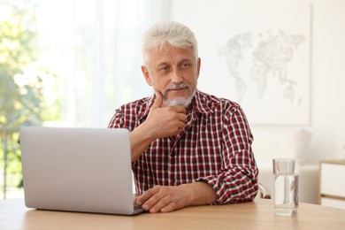 Photo of Senior man with laptop and glass of water at table indoors