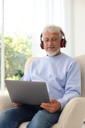 Photo of Senior man in headphones using laptop at home