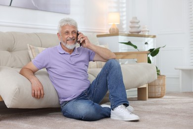 Photo of Smiling senior man talking on phone at home