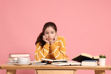 Photo of Preparing for exam. Student with books at table against pink background