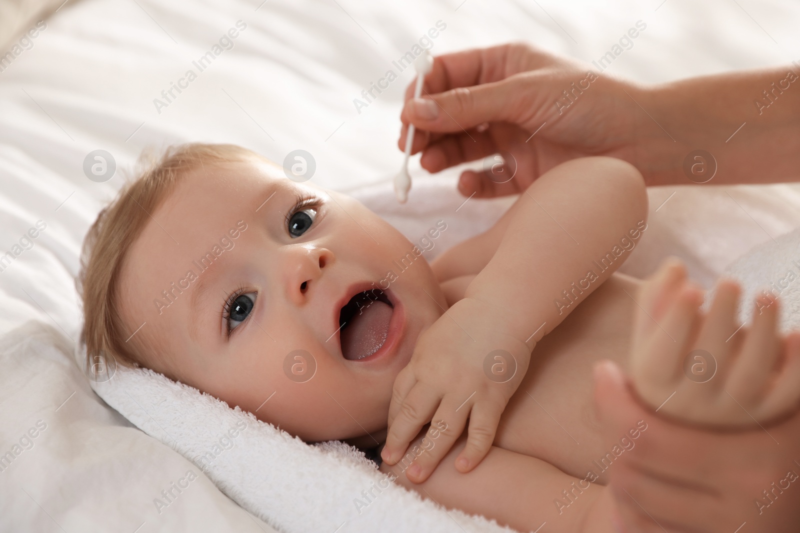 Photo of Mother cleaning ear of her cute little baby with cotton swab on bed, closeup