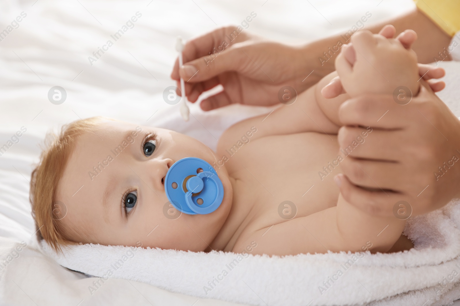 Photo of Mother cleaning ear of her cute little baby with cotton swab on bed, closeup