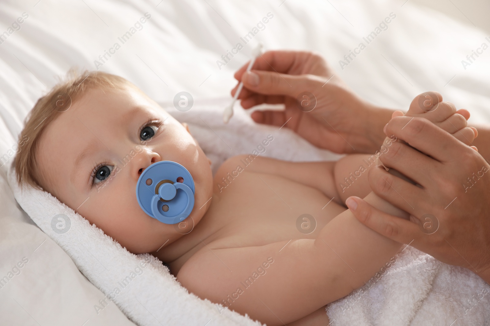 Photo of Mother cleaning ear of her cute little baby with cotton swab on bed, closeup