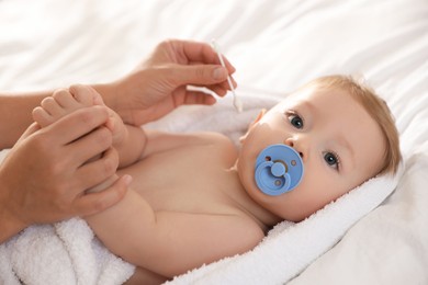 Photo of Mother cleaning ear of her cute little baby with cotton swab on bed, closeup