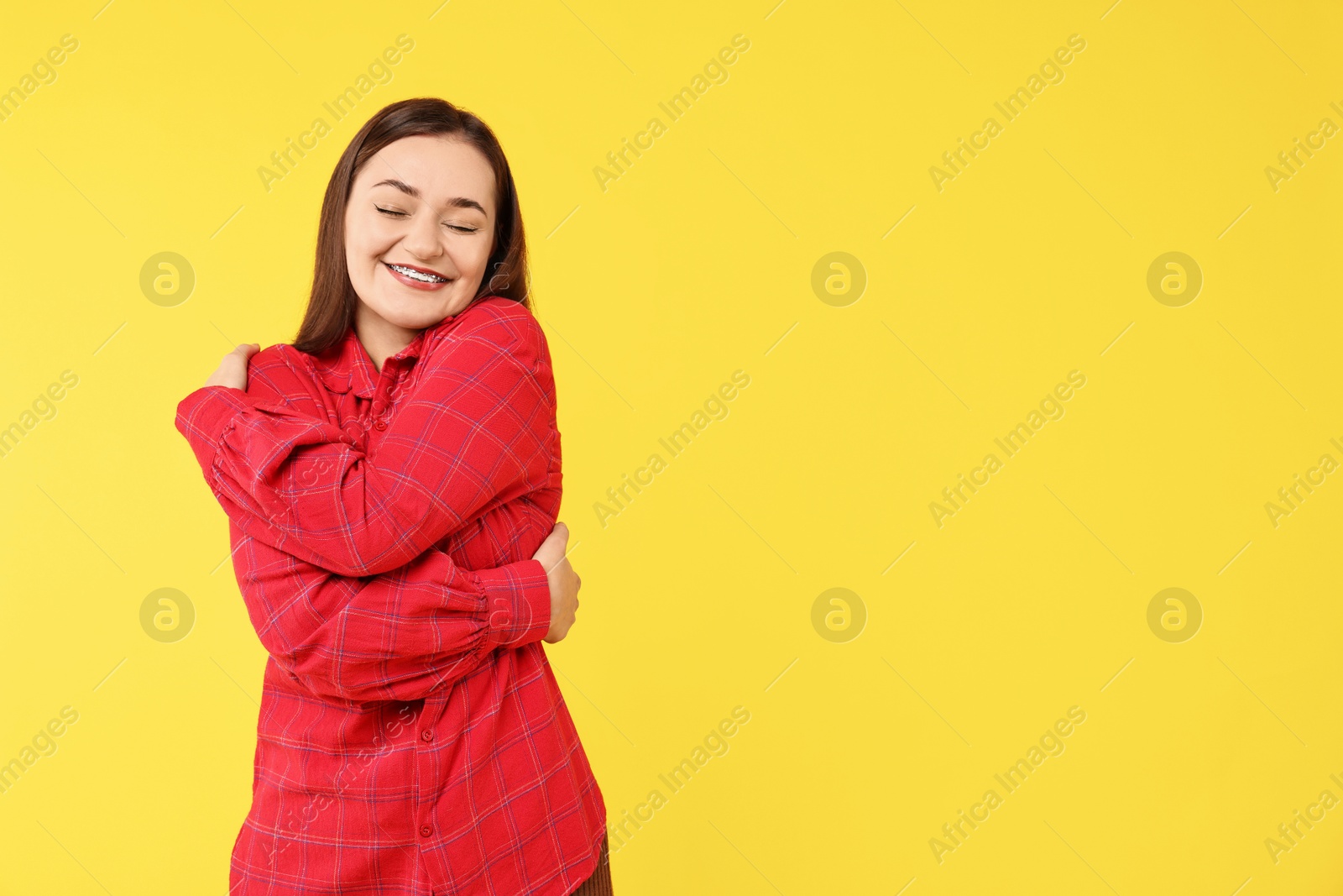 Photo of Beautiful young woman hugging herself on yellow background, space for text