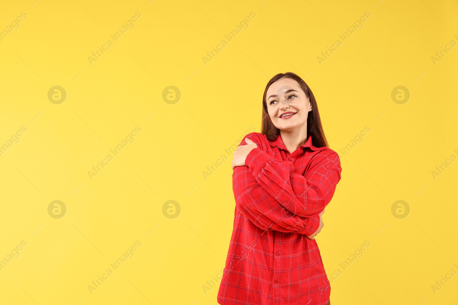 Photo of Beautiful young woman hugging herself on yellow background, space for text