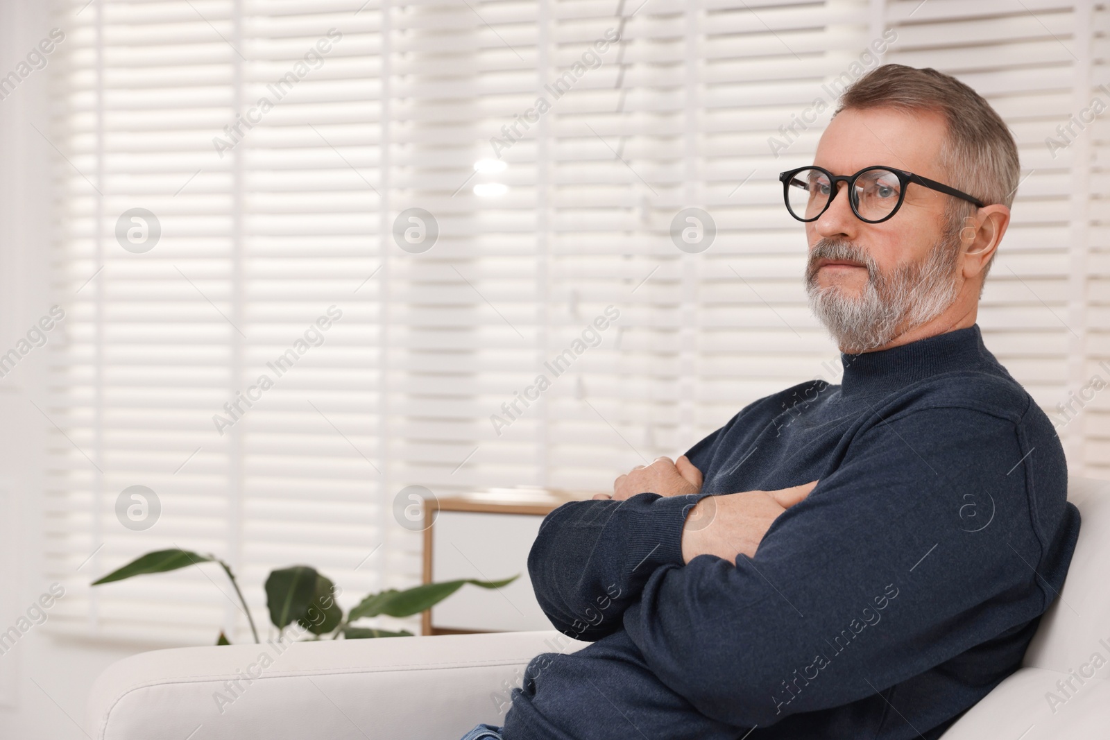 Photo of Mature man with crossed arms at home. Space for text