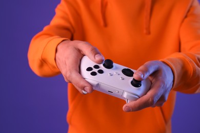 Photo of Man playing video games with controller on violet background, closeup