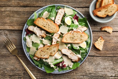 Photo of Tasty Caesar salad with chicken served on wooden table, flat lay