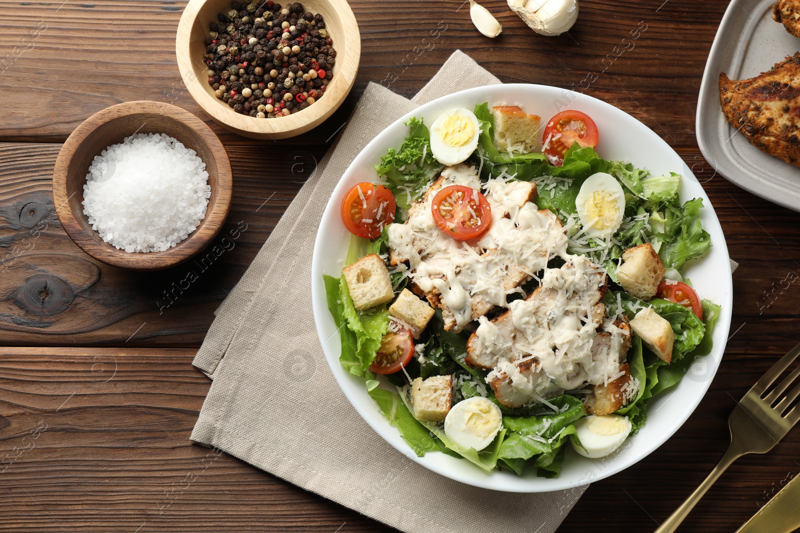 Photo of Tasty Caesar salad with chicken and tomatoes in bowl served on wooden table, flat lay