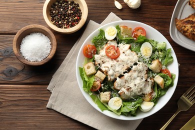 Photo of Tasty Caesar salad with chicken and tomatoes in bowl served on wooden table, flat lay