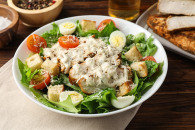 Photo of Tasty Caesar salad with chicken and tomatoes in bowl on wooden table, closeup