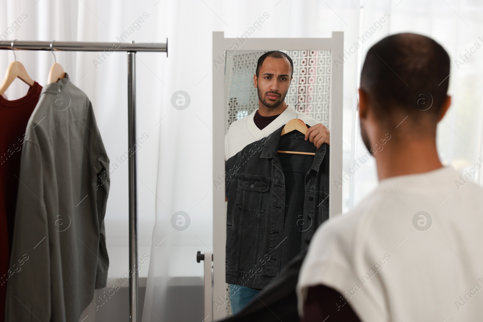 Photo of Handsome man choosing clothes near mirror at home