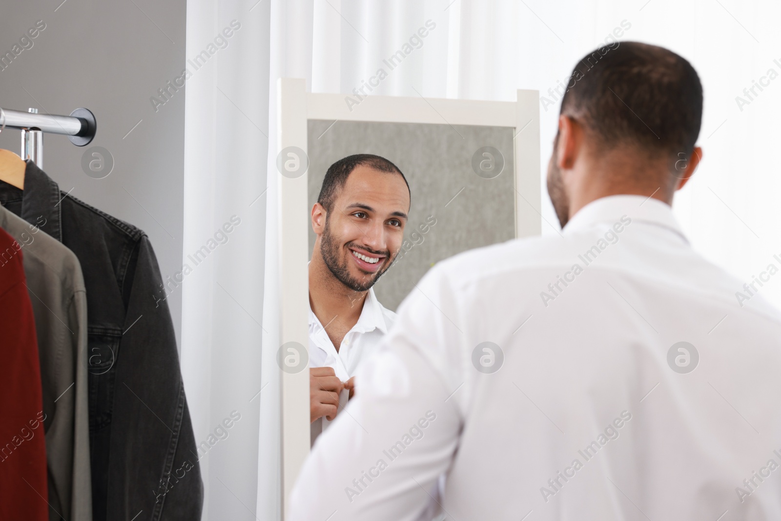 Photo of Smiling man dressing near mirror at home, back view