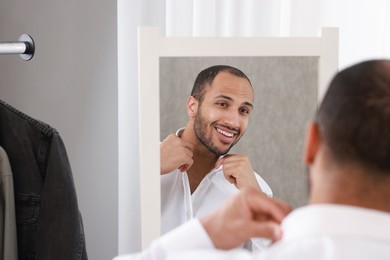 Photo of Smiling man dressing near mirror at home