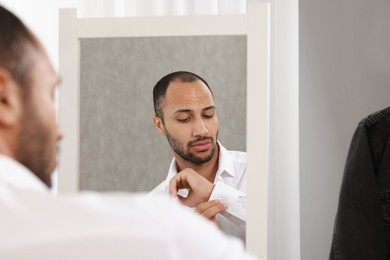 Photo of Handsome man dressing near mirror at home