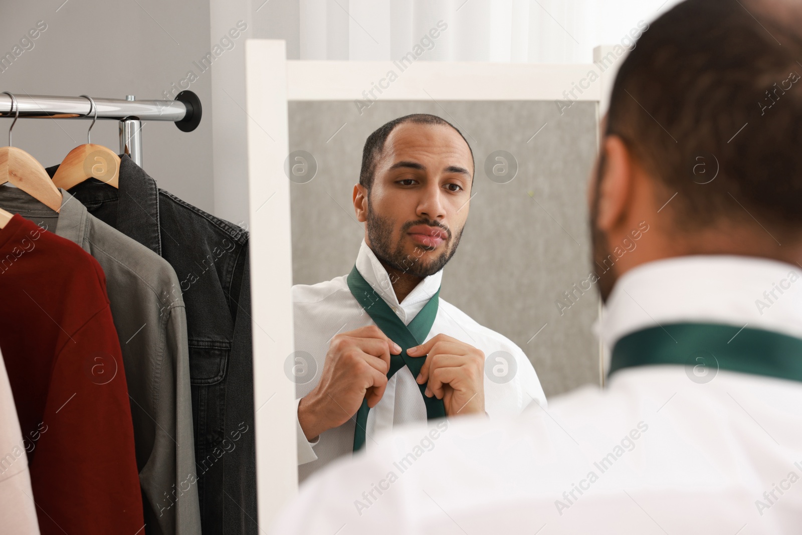 Photo of Handsome man adjusting necktie near mirror at home