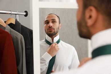 Photo of Handsome man adjusting necktie near mirror at home