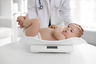 Photo of Pediatrician weighting little child in clinic, closeup. Checking baby's health