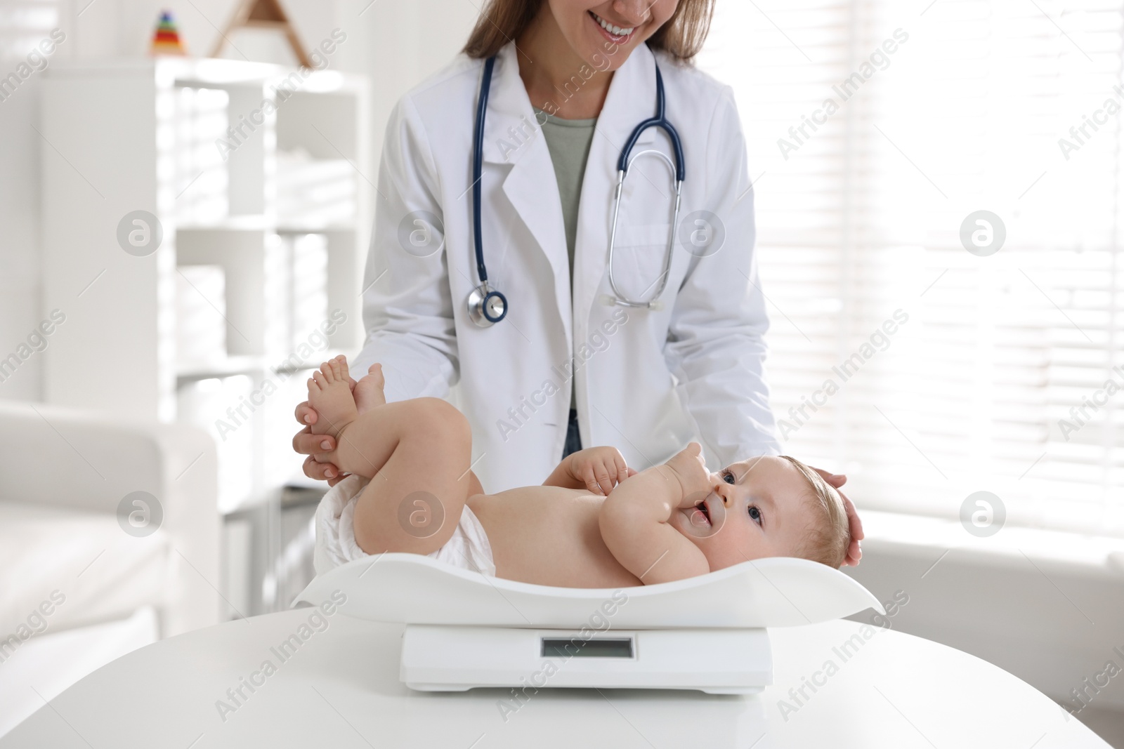 Photo of Pediatrician weighting little child in clinic, closeup. Checking baby's health