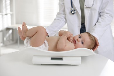 Photo of Pediatrician weighting little child in clinic, closeup. Checking baby's health