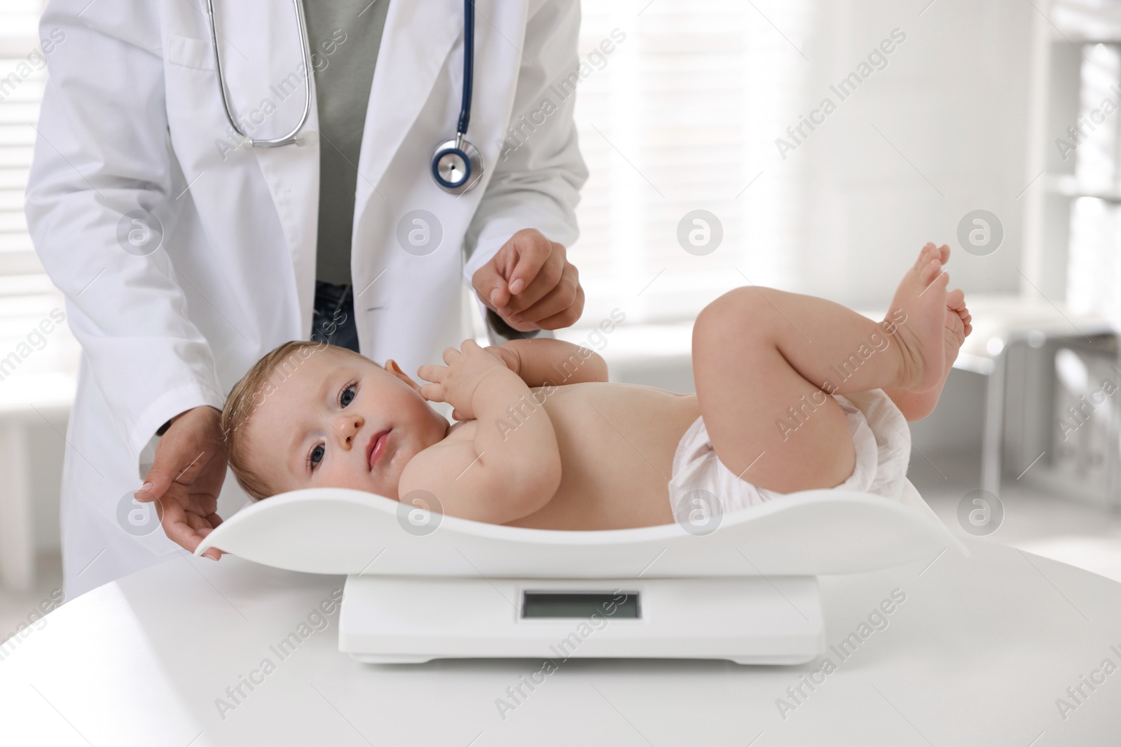 Photo of Pediatrician weighting little child in clinic, closeup. Checking baby's health