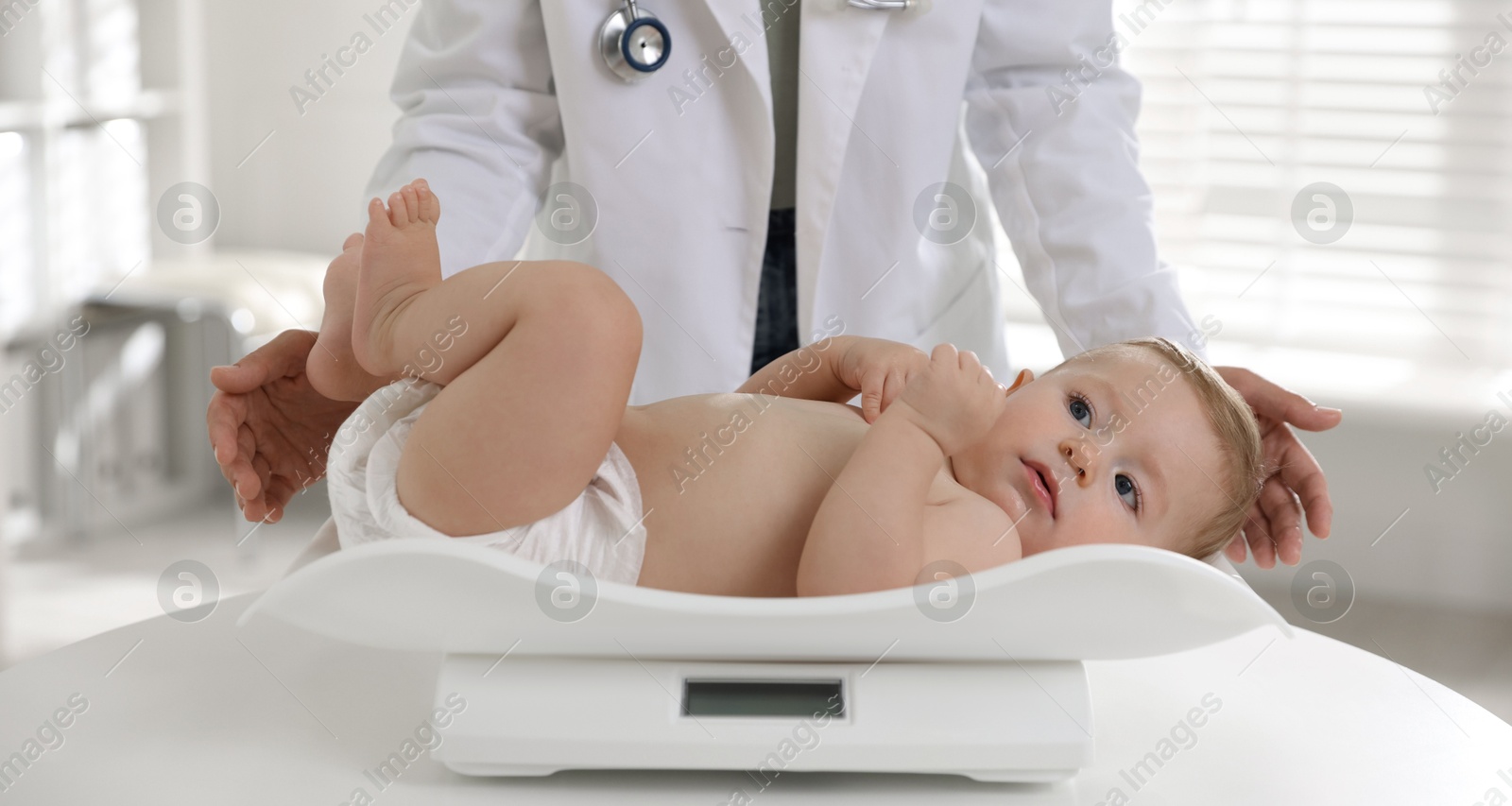 Photo of Pediatrician weighting little child in clinic, closeup. Checking baby's health