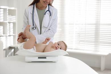 Photo of Pediatrician weighting little child in clinic, closeup. Checking baby's health