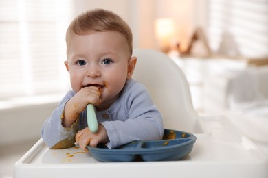 Photo of Cute little baby eating healthy food in high chair indoors