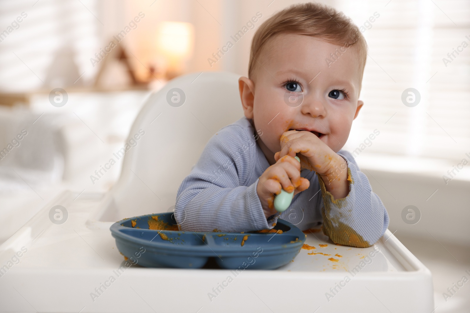 Photo of Cute little baby eating healthy food in high chair indoors