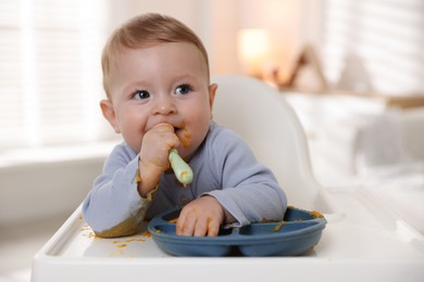 Photo of Cute little baby eating healthy food in high chair indoors