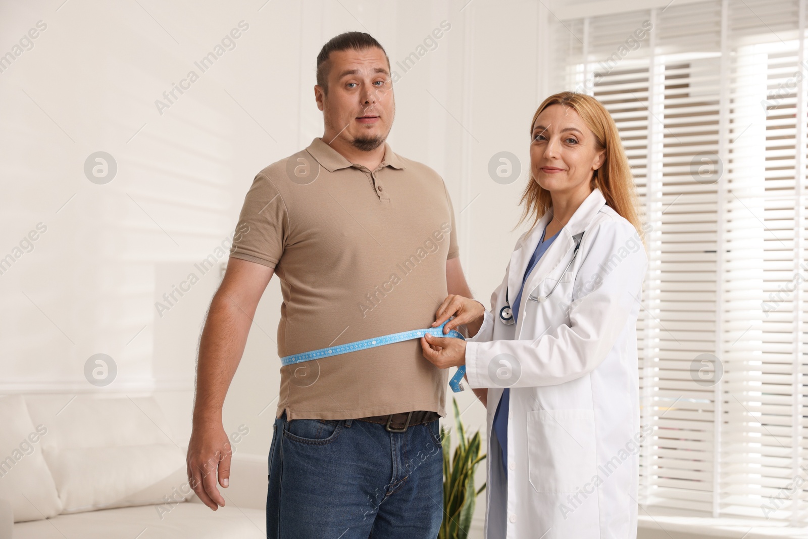 Photo of Nutritionist measuring overweight man's waist with tape in clinic