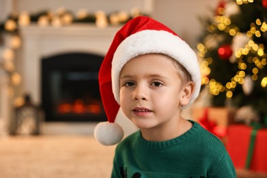 Photo of Cute little boy with Santa hat in room decorated for Christmas, space for text