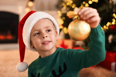 Photo of Cute little boy in Santa hat with Christmas ball at home