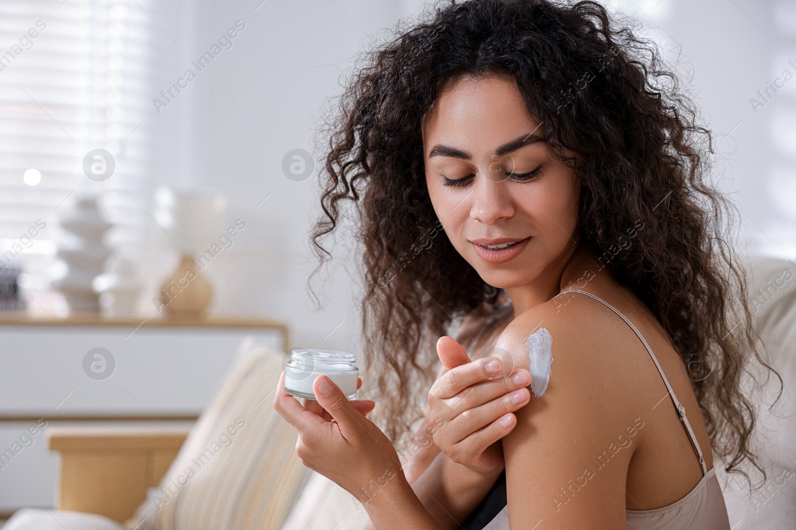 Photo of Young woman applying cream onto shoulder at home. Space for text