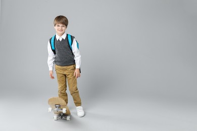 Photo of Little boy with skateboard on light grey background, space for text