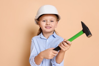 Photo of Little girl in hard hat with hammer on beige background. Dreaming about future profession