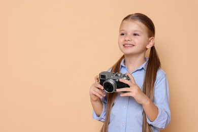 Photo of Little girl with camera pretending to be photographer on beige background, space for text. Dreaming of future profession