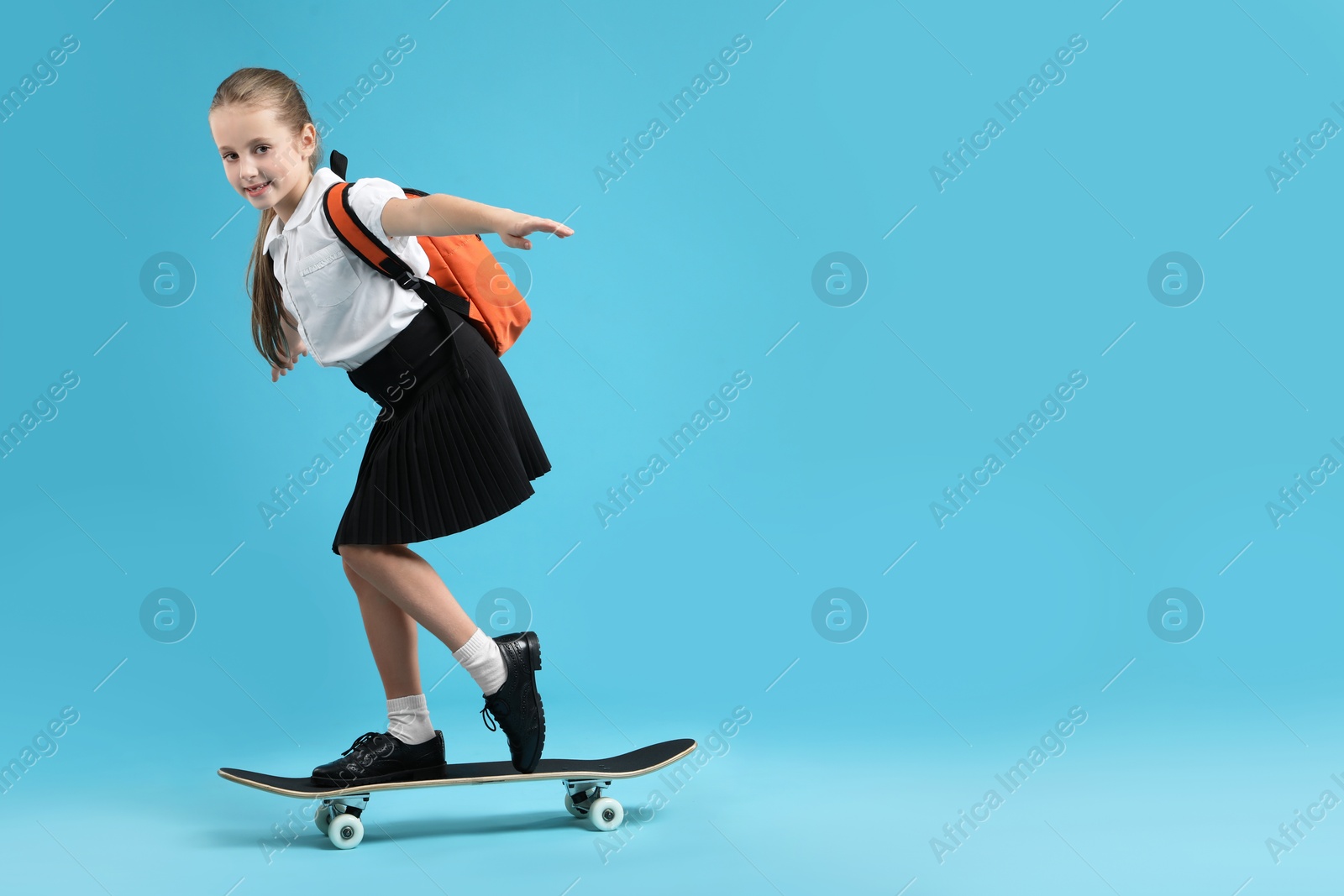 Photo of Little girl standing on skateboard against light blue background, space for text