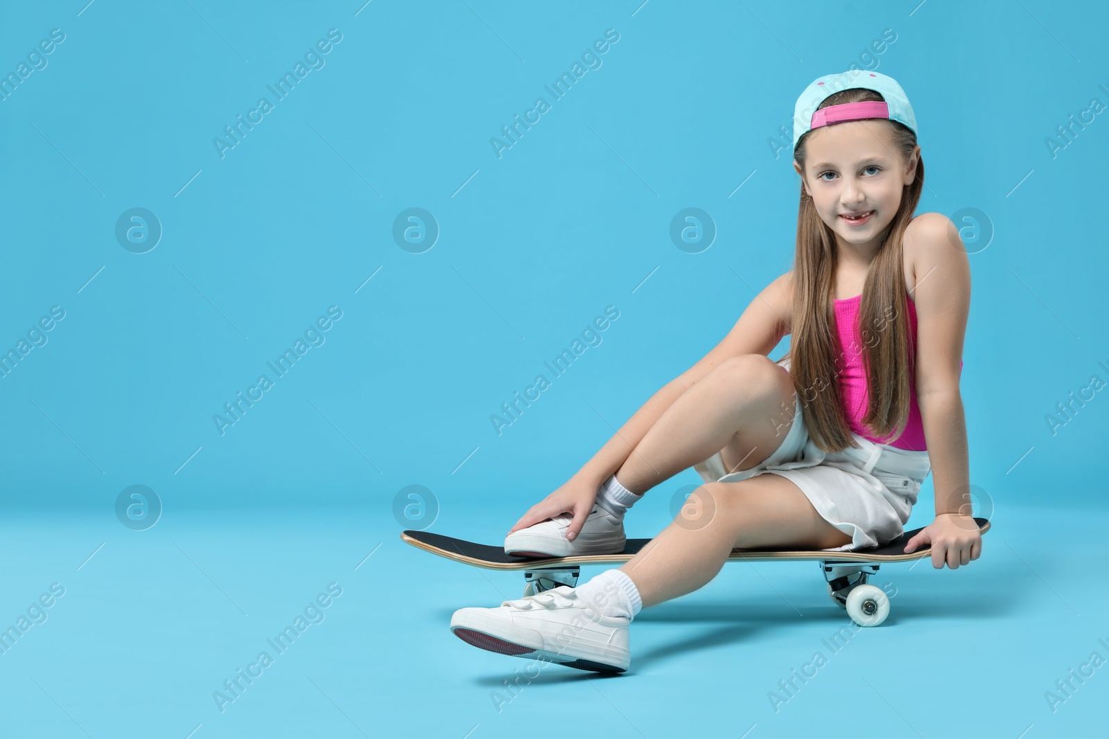 Photo of Stylish girl sitting on skateboard against light blue background, space for text