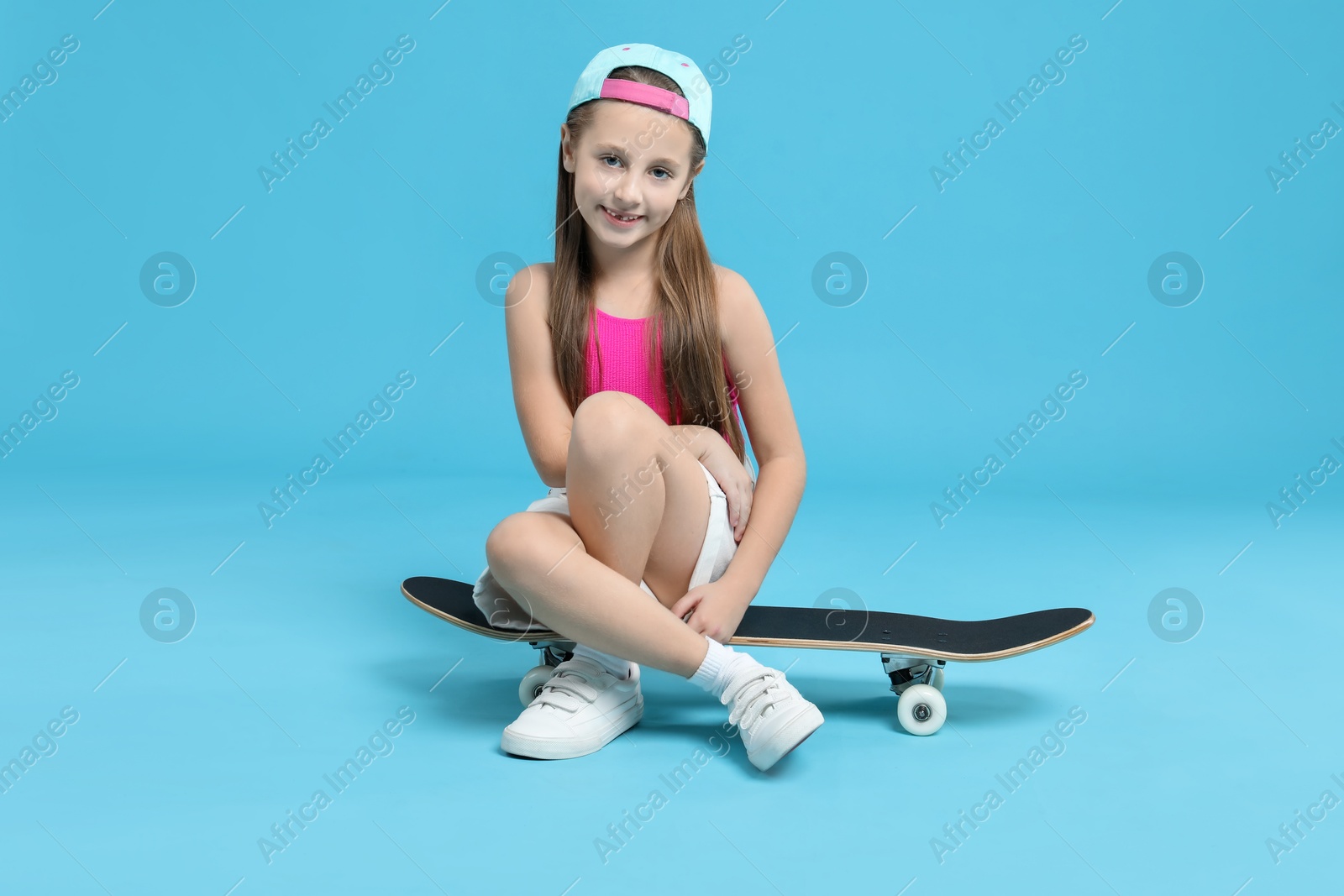 Photo of Stylish girl sitting on skateboard against light blue background