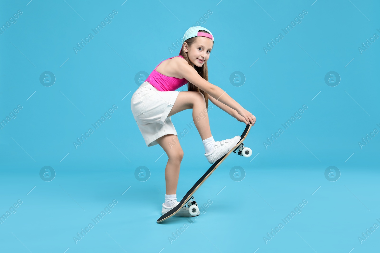 Photo of Stylish girl with skateboard on light blue background