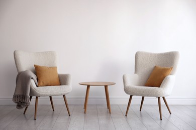 Photo of Soft armchairs and coffee table near white wall indoors