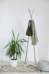 Photo of Macrame bag with fruits and jacket on clothing rack indoors