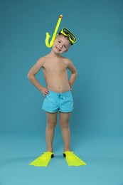 Photo of Cute little boy in beachwear with snorkeling equipment on light blue background