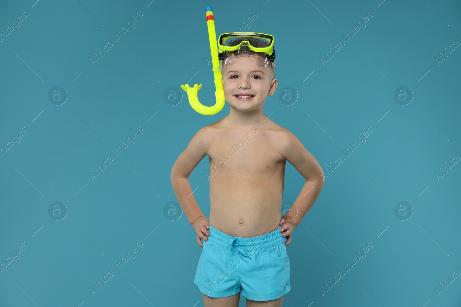 Photo of Cute little boy in beachwear with snorkeling equipment on light blue background