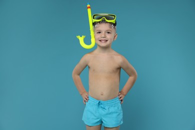 Photo of Cute little boy in beachwear with snorkeling equipment on light blue background