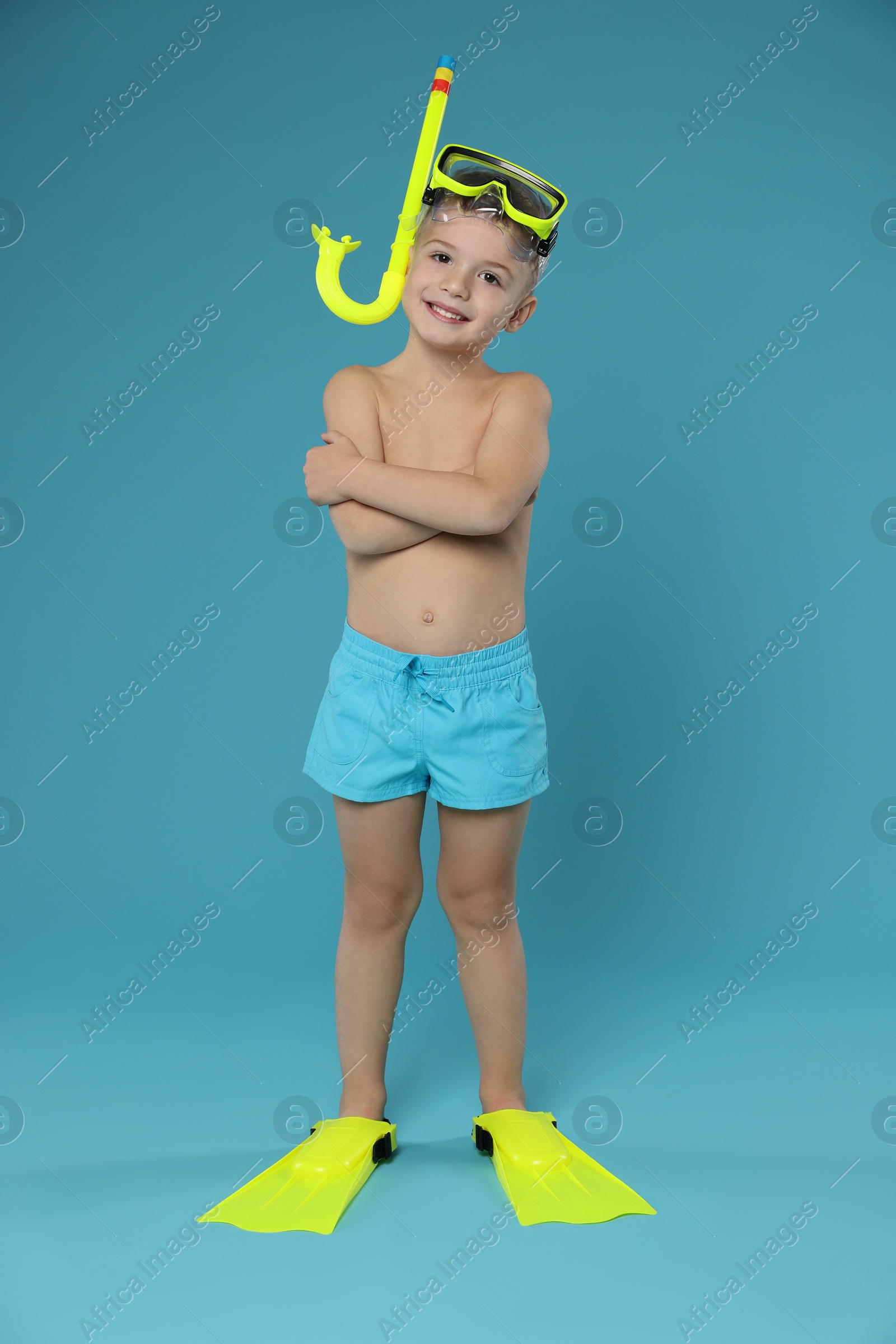 Photo of Cute little boy in beachwear with snorkeling equipment on light blue background