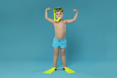 Photo of Cute little boy in beachwear with snorkeling equipment on light blue background