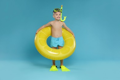 Photo of Cute little boy in beachwear with snorkeling equipment and inflatable ring on light blue background